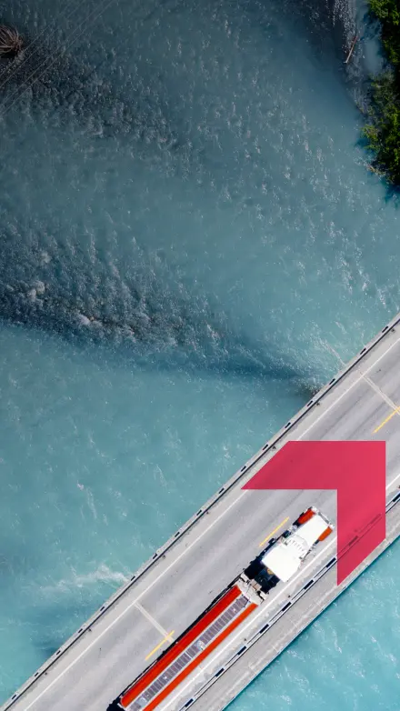 Aerial view of a semi-truck driving across a bridge over blue water representing commercial truck insurance services by GIA Group, LLC