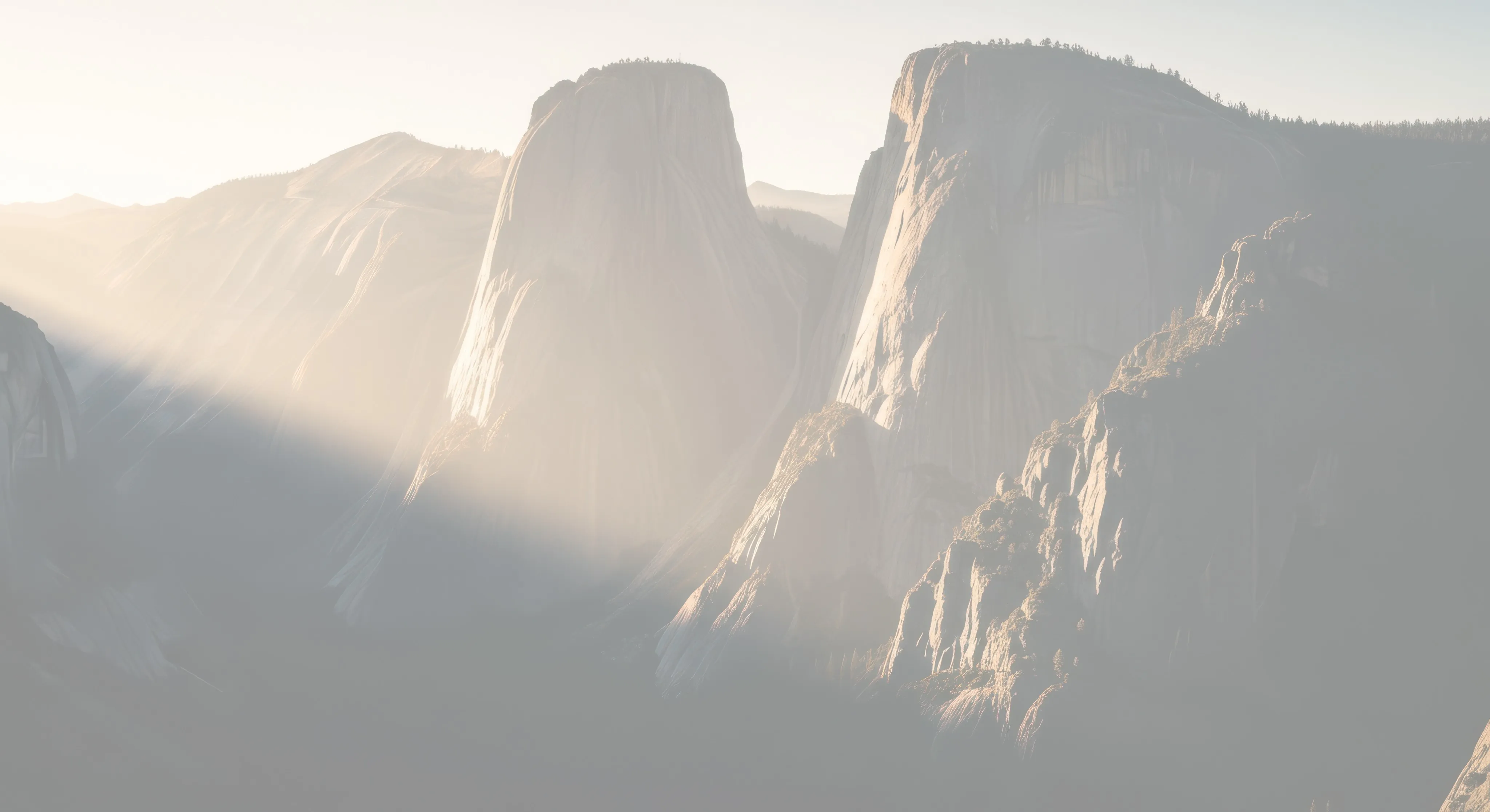 Sunrise over hills, casting golden rays and shadows across rugged cliffs. The scene conveys tranquility and natural grandeur.