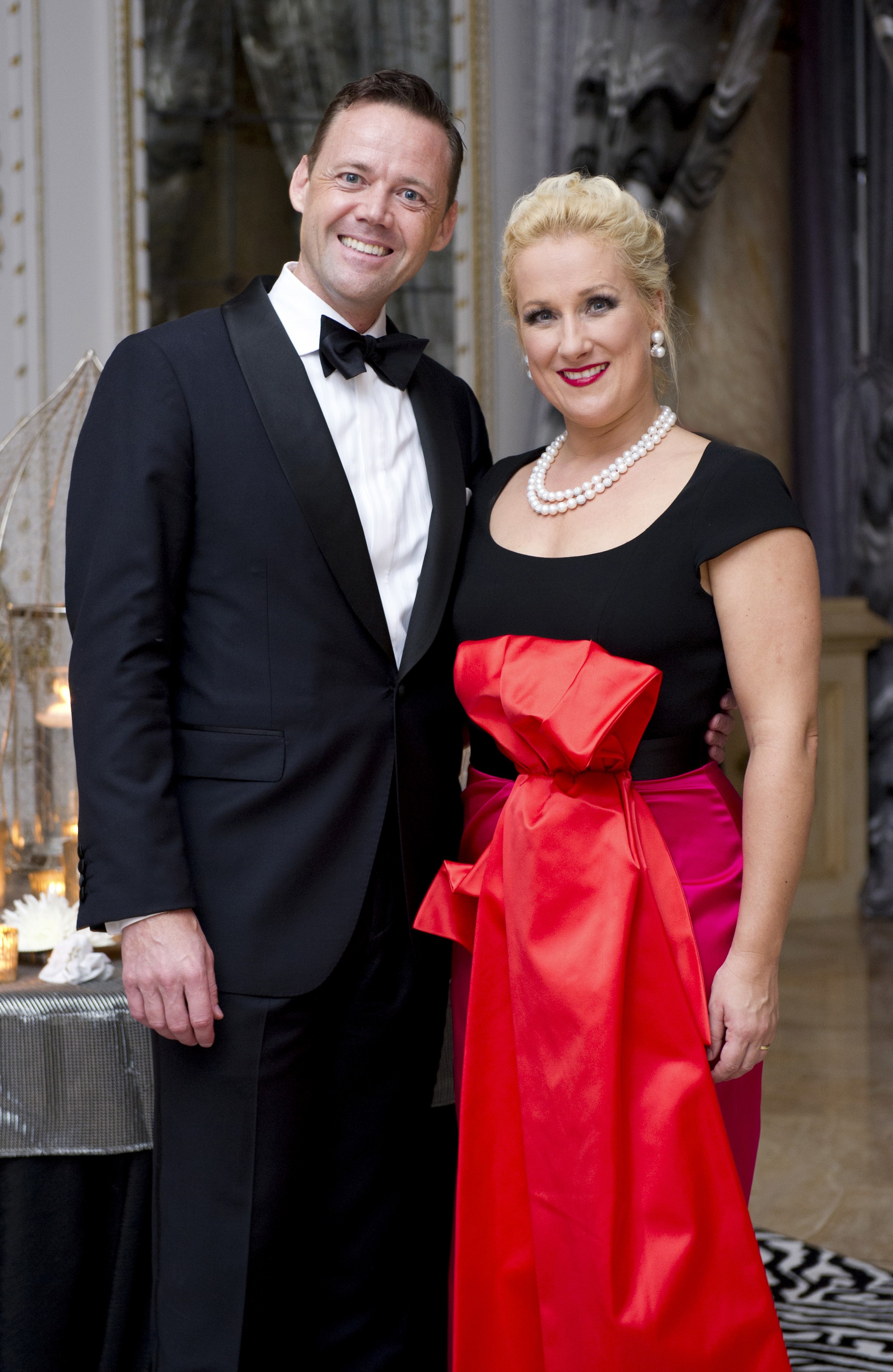 A blond woman in a black and red gown and a man in a tuxedo smile after a Gala performance.