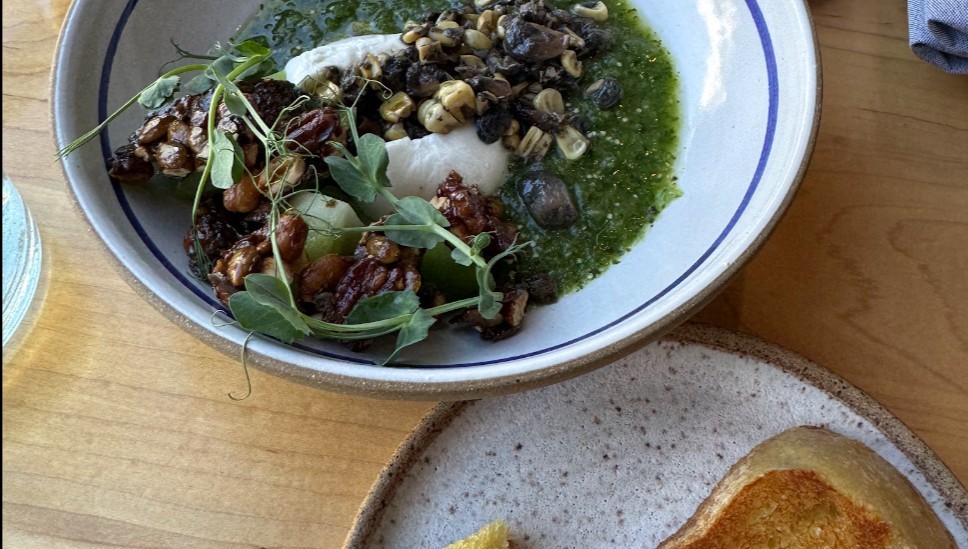 A dish of burrato and sliced sour dough bread, served on white dishes atop a wooden table at Mezcaleria Alma.