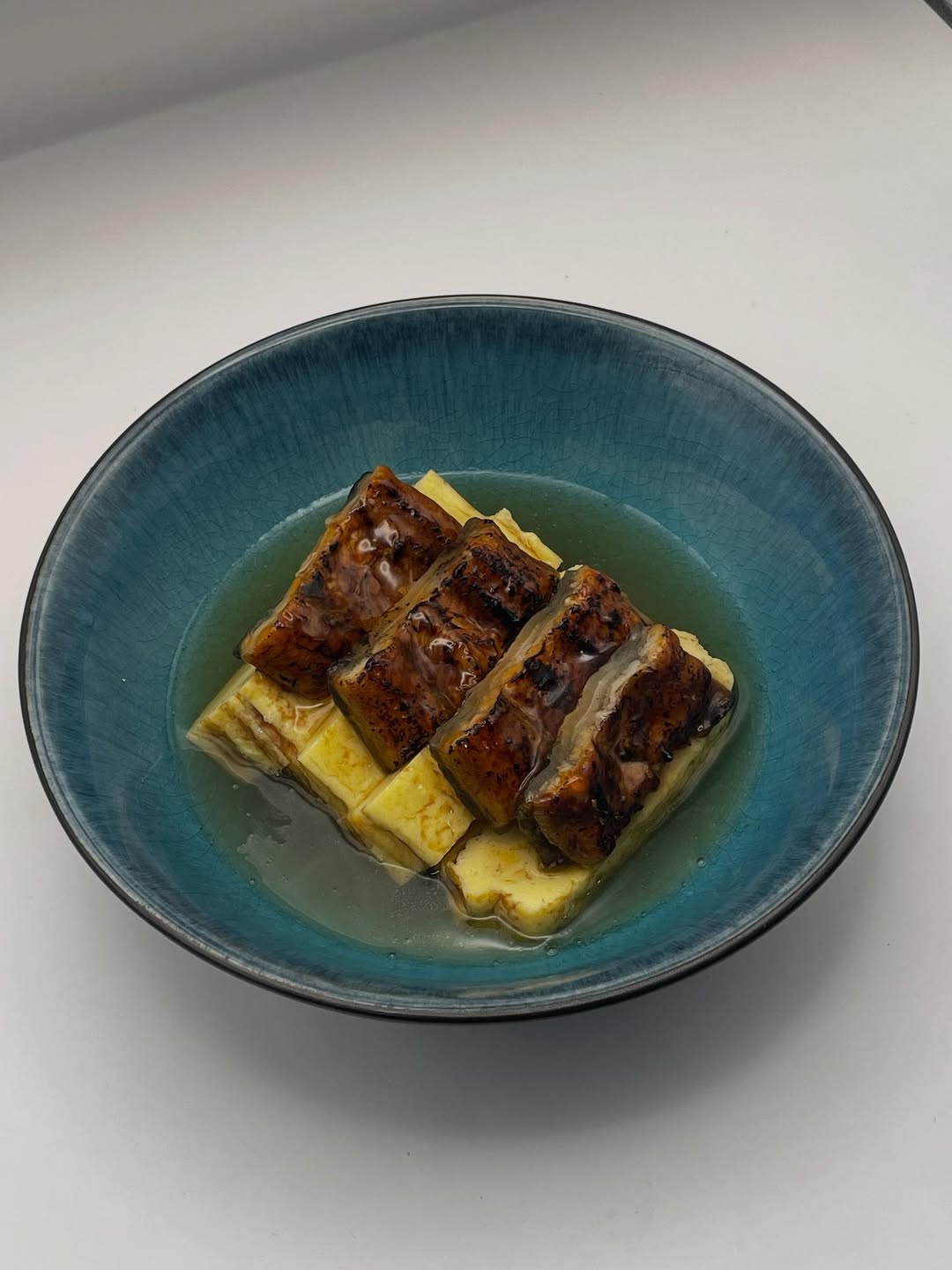 Restaurant interior with wooden tables and chairs lined against a textured wall, softly lit by round wall lamps.