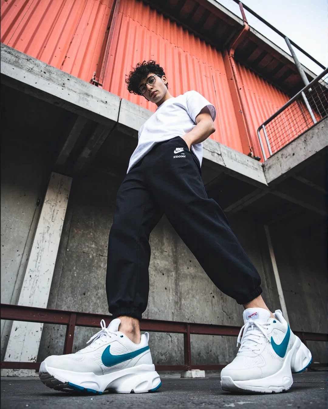 Low-angle urban fashion photograph showcasing white and teal sneakers against concrete and orange metal backdrop with street style aesthetic