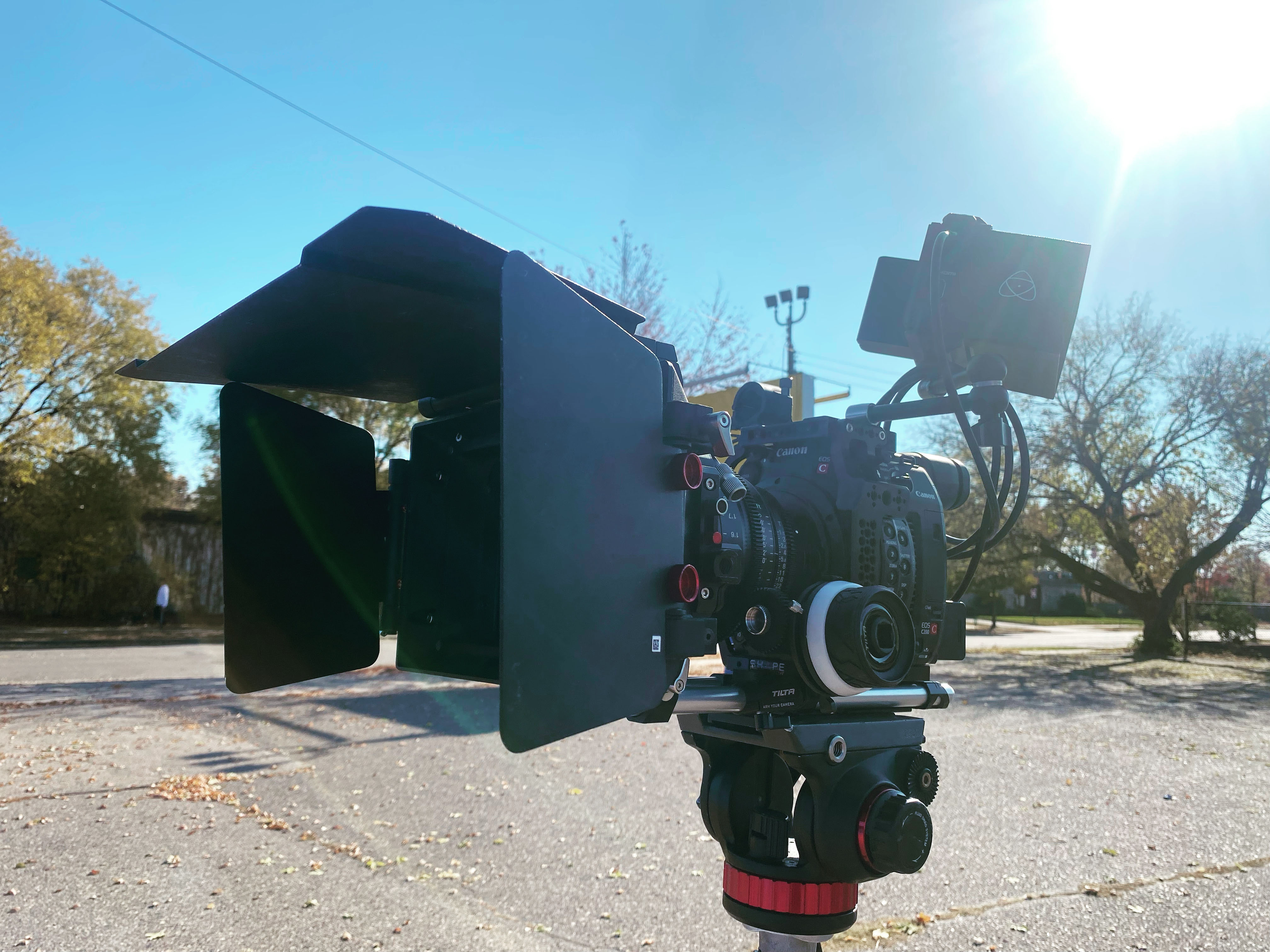 Professional cinema camera rig with a matte box and external monitor mounted on a tripod outdoors.