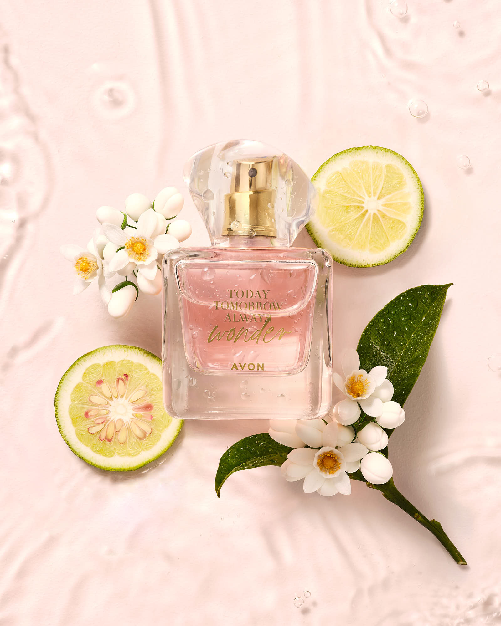 Avon fragrance bottle with pink liquid, surrounded by fresh citrus slices and white flowers on a light pink background.