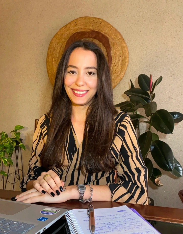 Smiling female therapist with short gray hair, wearing a brown top and a purple shawl, surrounded by a cozy background.