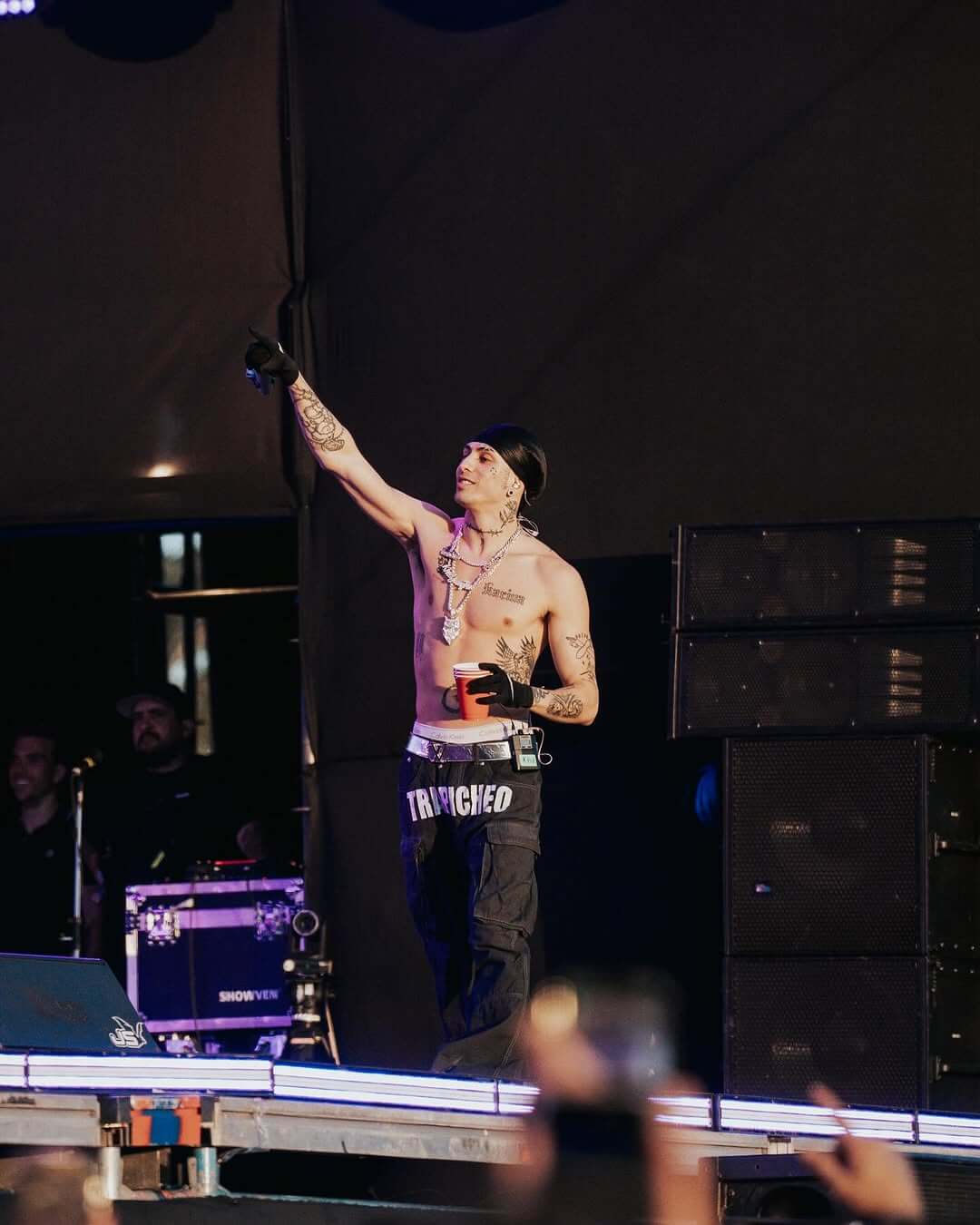 KHEA sin camisa en un concierto, levantando el brazo y animando al público.