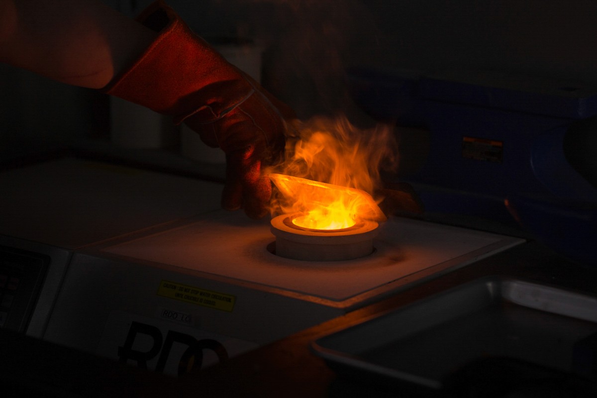Industrial precious metals refining process showing molten gold being poured into a crucible.