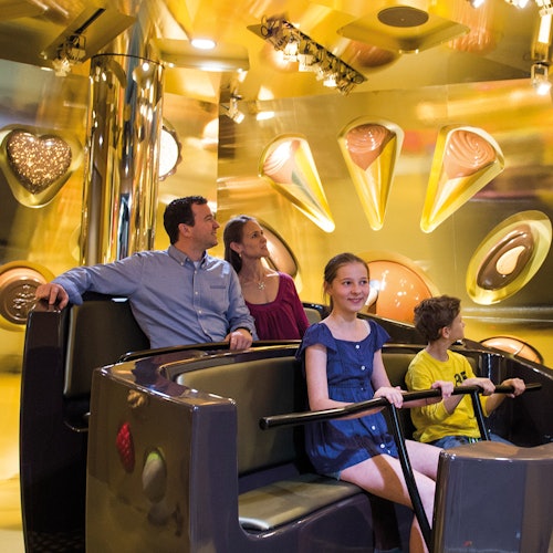 A family of four rides an amusement park attraction with chocolate decorations on the wall in the background.
