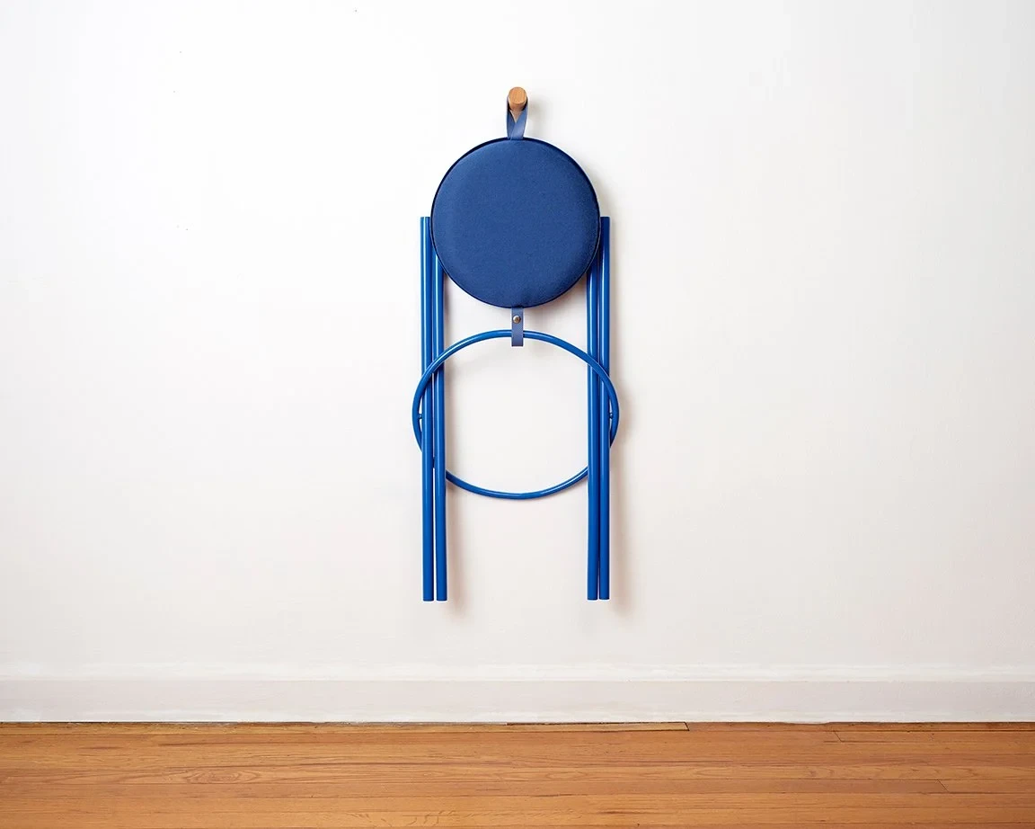 Blue collapsible hanging stool folded vertically against a white wall