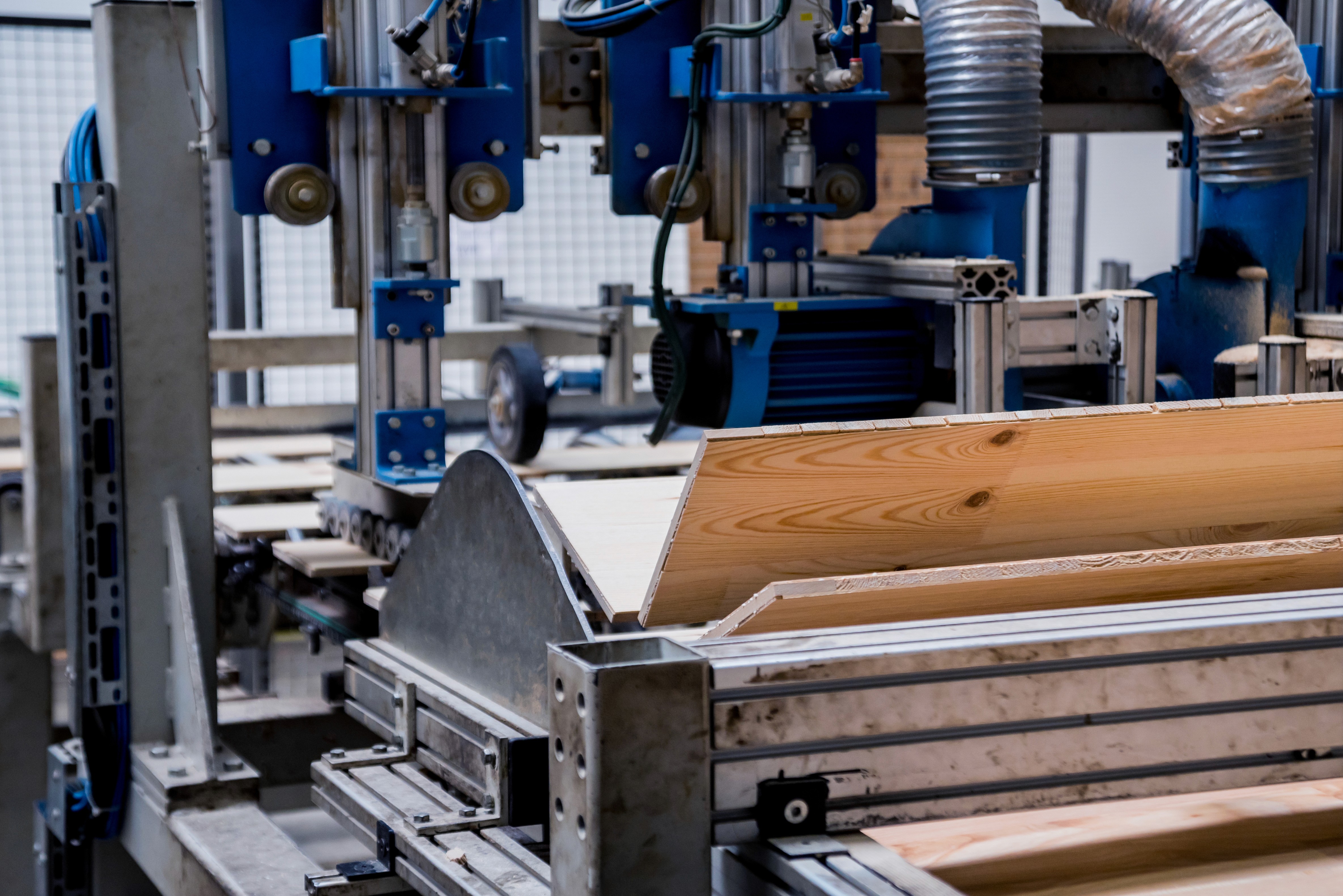 Close-up of woodworking machinery with wooden planks in the foreground, showcasing tools and equipment in use.