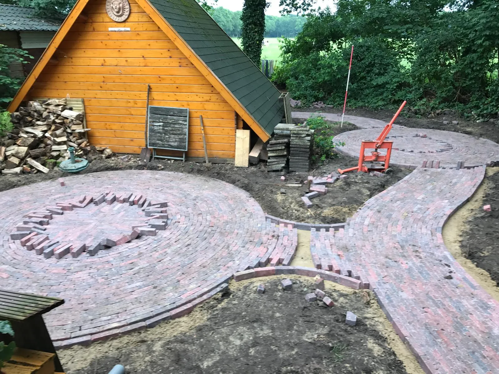 Ronde en slingerende tuinpaden van gebakken klinkers in aanleg bij houten tuinschuur in Terwispel