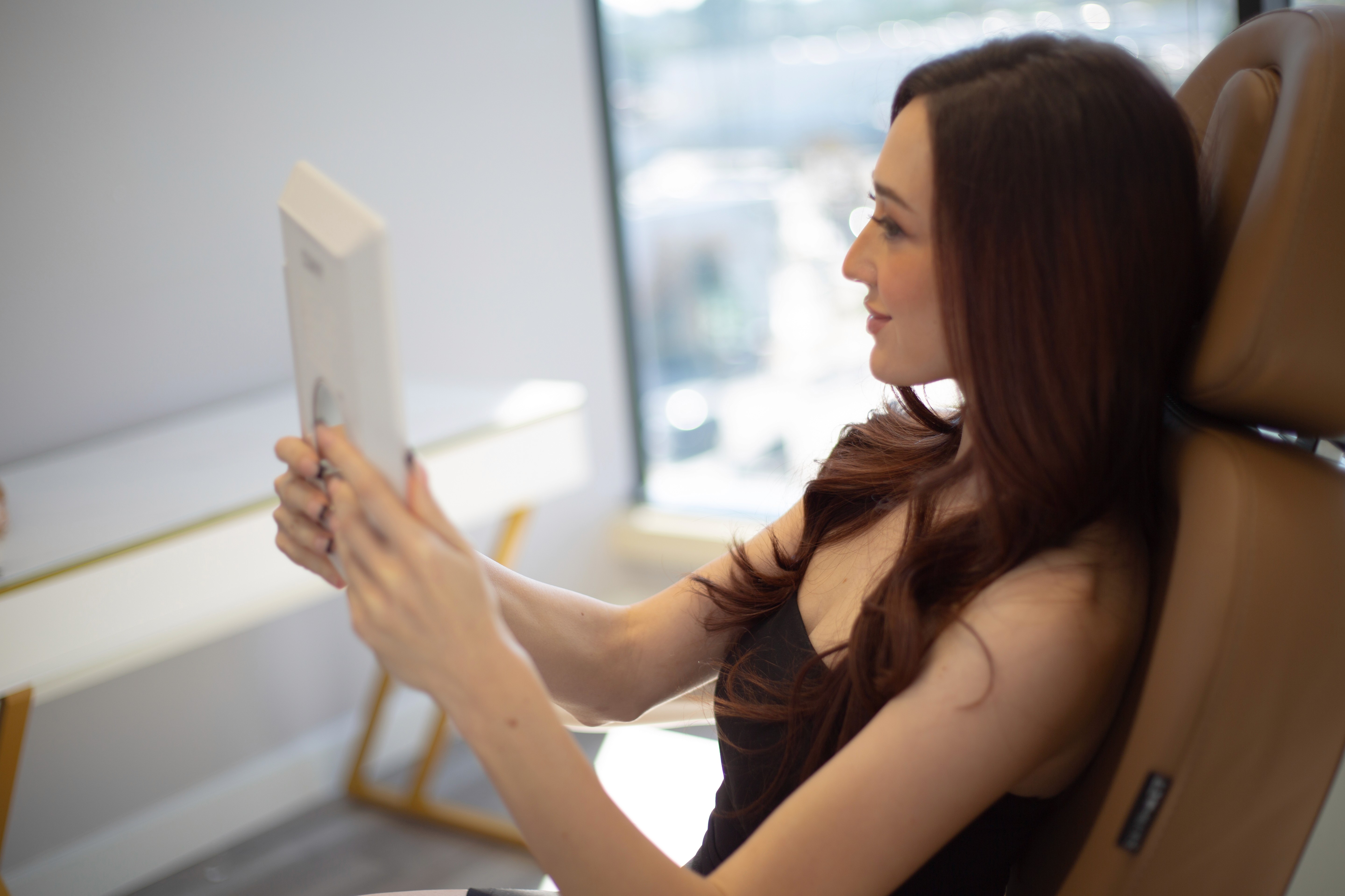 Person holding a handheld mirror while seated in a bright treatment room.