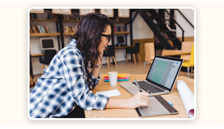 Woman working on laptop using graphic tablet in creative workspace