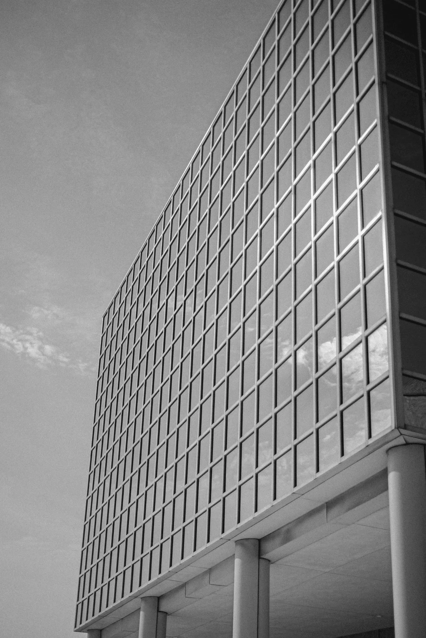 Black and white low-angle view of a modern building's glass grid facade against a clear sky.