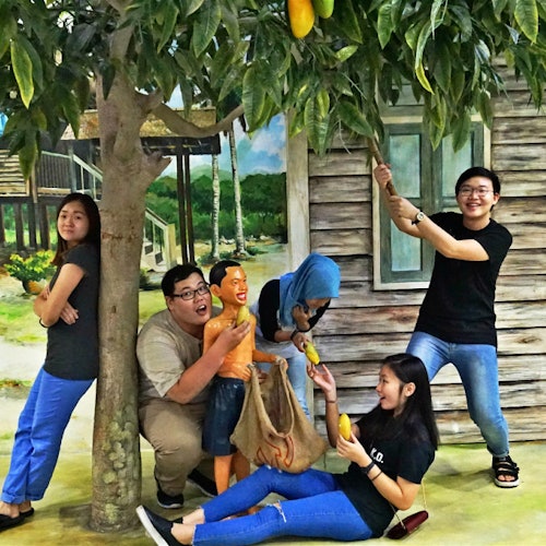 五个人在一棵芒果树旁嬉戏,其中一些人正在拿着或伸手抓取芒果,背景是一个古朴的建筑物。