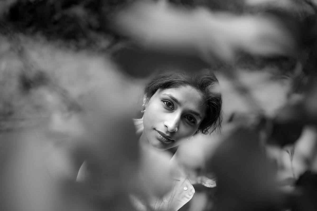 Young woman peeking through blurred leaves — editorial portraiture image 10 for "A Study in Poise"