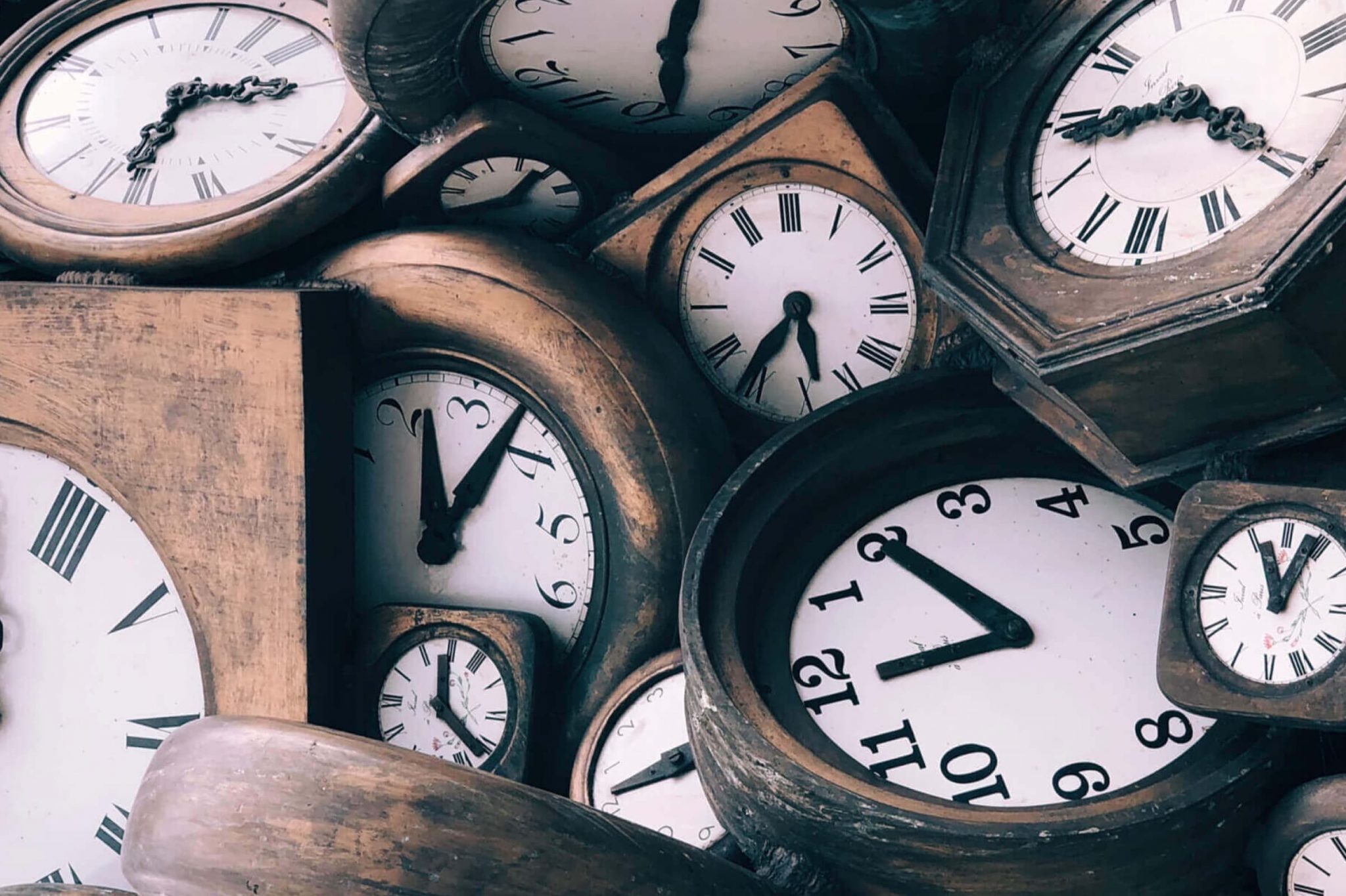 A pile of analogue clocks displaying different times