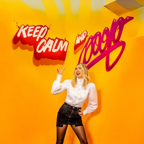 A smiling woman poses in front of a bright yellow background featuring the text "KEEP CALM AND 10000" in red and purple lettering.