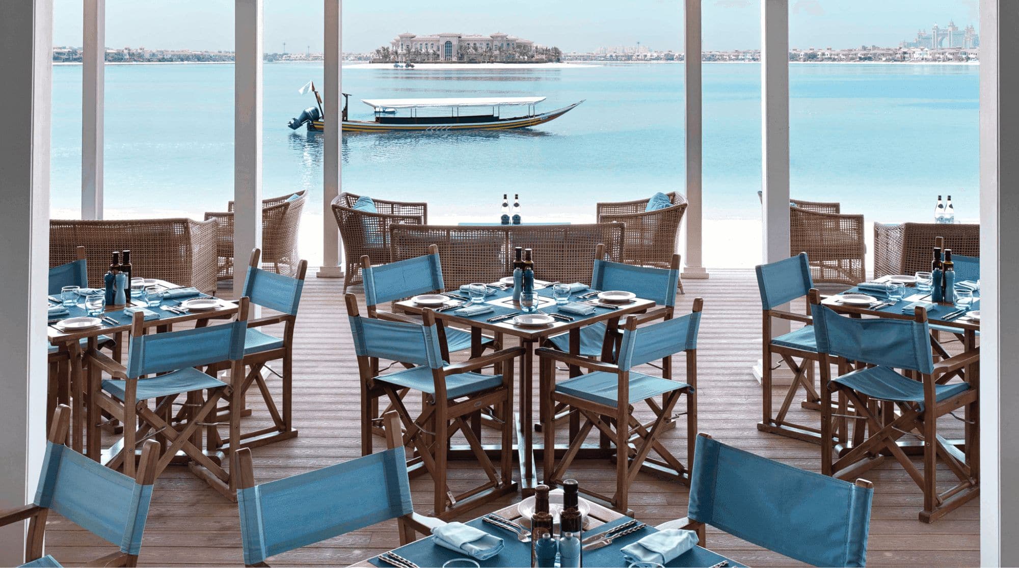 The Beach House, a beachfront restaurant that features wooden floors, tables, and chairs, with a blue aesthetic and spacious dining space.
