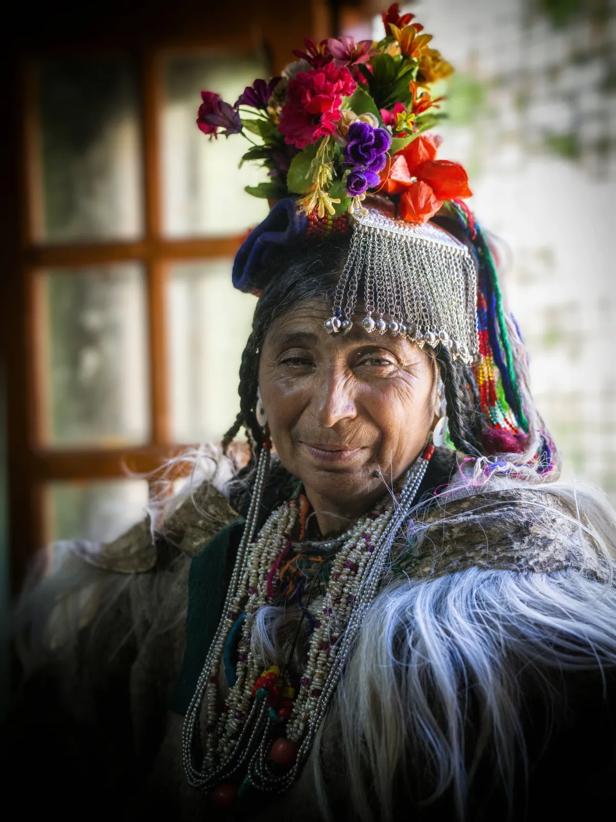 Anciana brokpa sonriente con tocado de flores y joyas de plata en Dha-Hanu