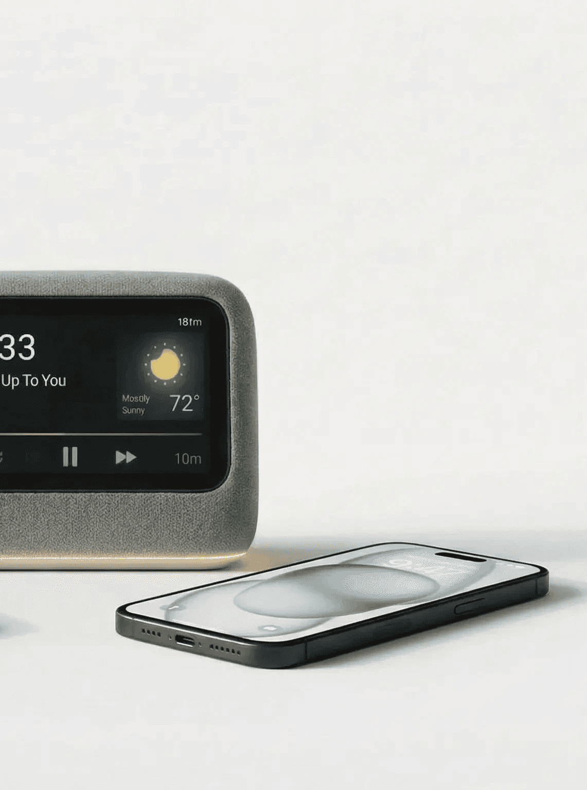 A digital clock with a weather display next to a smartphone on a light surface.