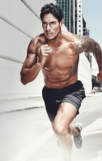 Muscular man running outdoors shirtless in an urban environment, showcasing strength, focus, and determination.