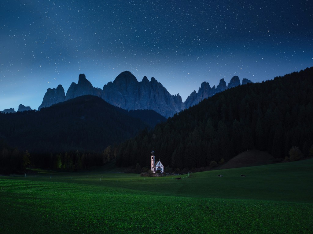 A chapel in a field with mountains in the distance at night