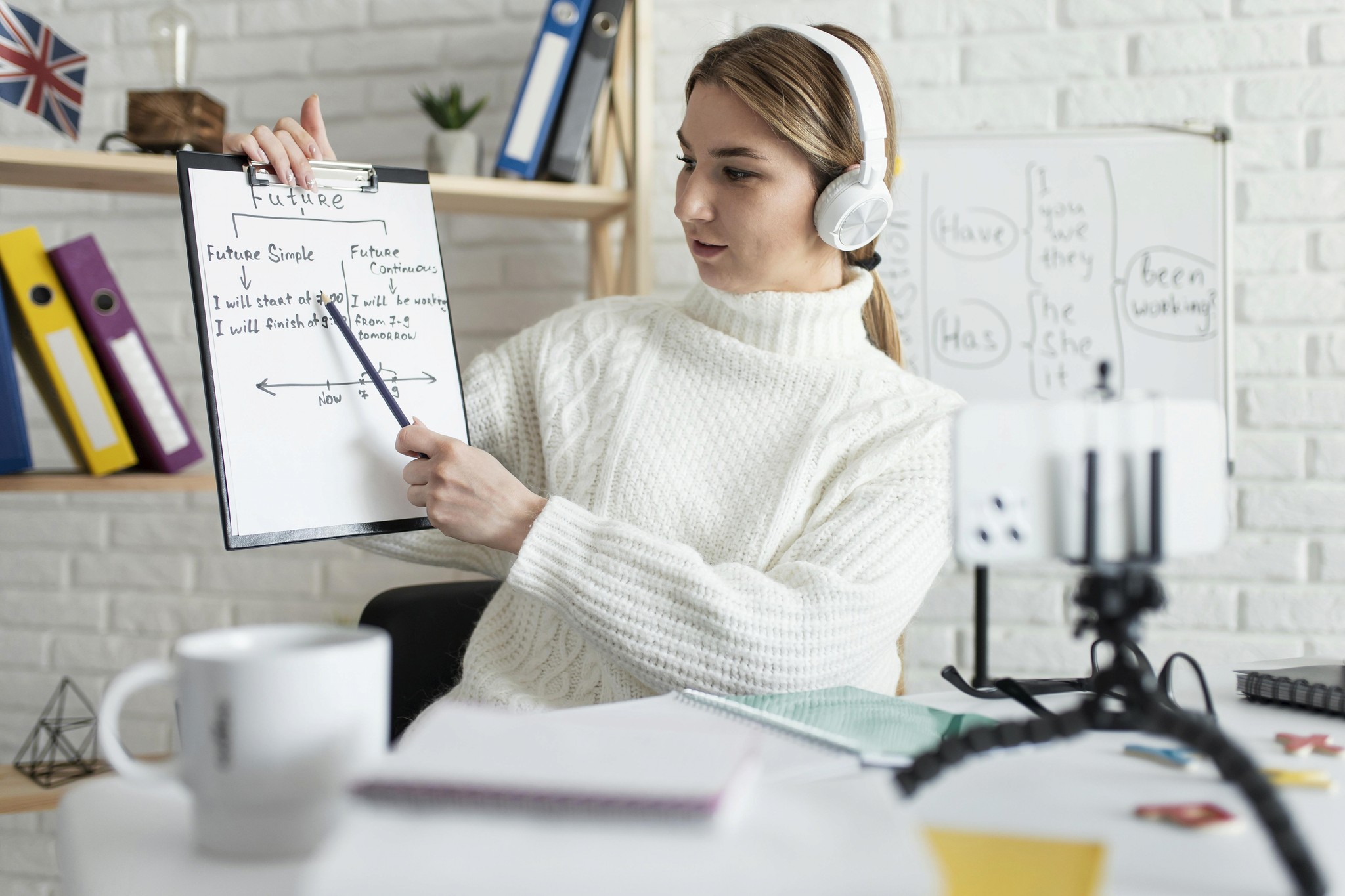 A woman seated at a desk, holding a clipboard, appears focused and engaged in her work.