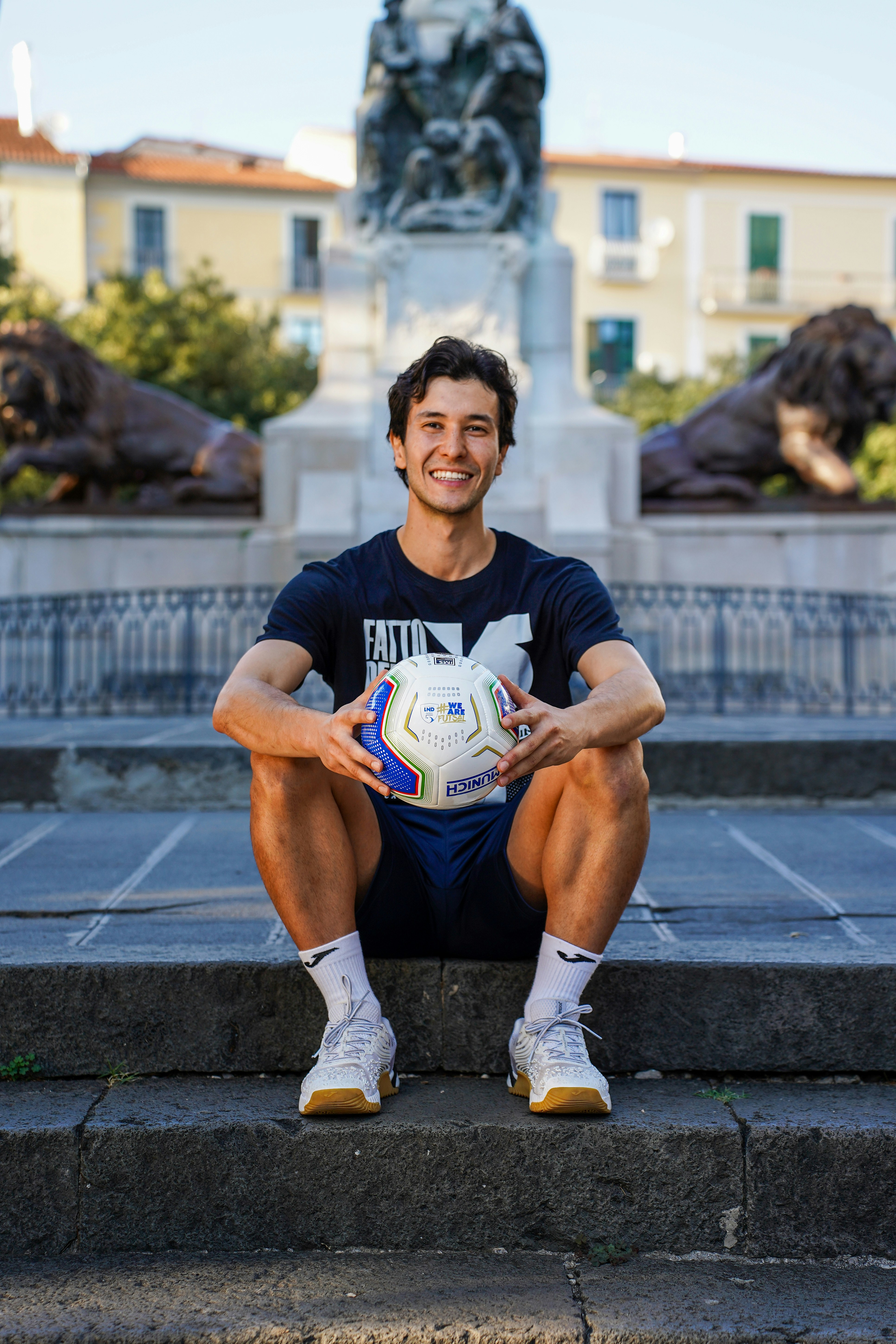 Man holding soccer ball sitting on stone steps.
