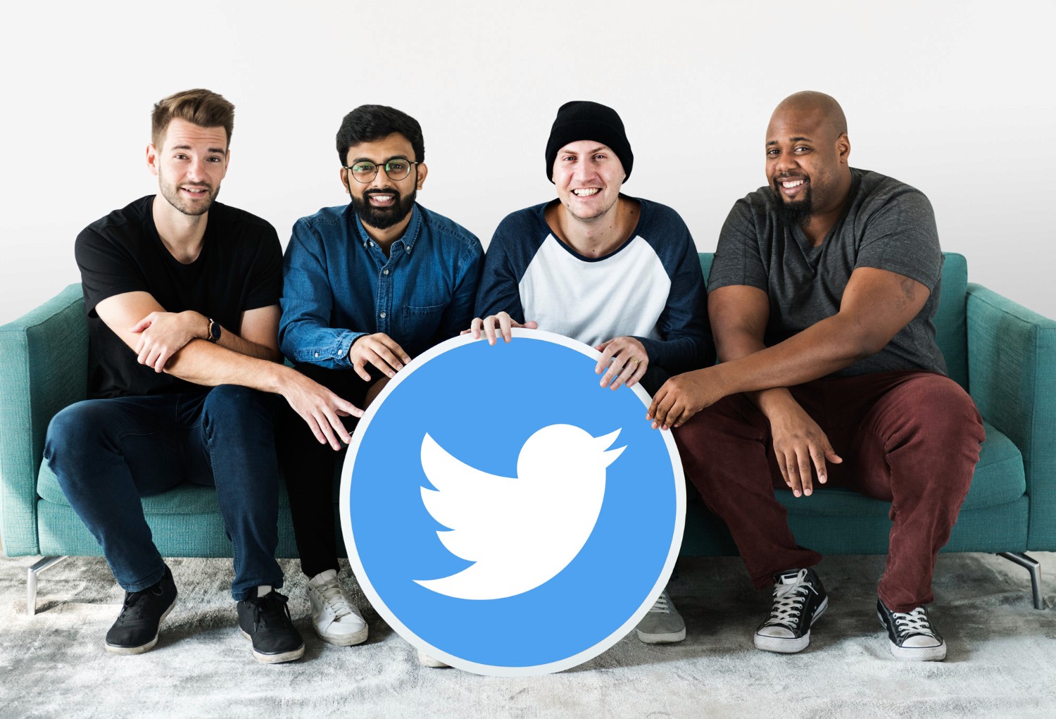 Four men seated on a couch, each holding a Twitter sign, smiling and engaging with one another.