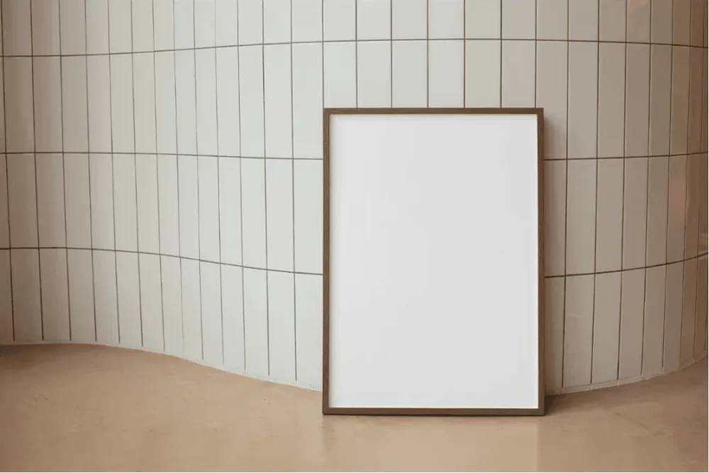 Mockup of a framed poster leaning against a tiled wall with a curved design. The warm, neutral tones and minimalist setting provide a modern, stylish presentation for showcasing artwork or branding.