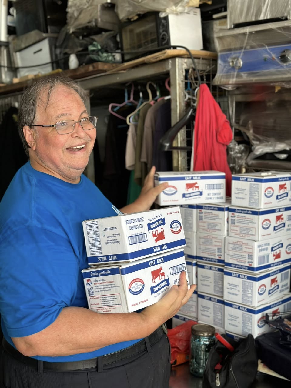 man in blue t-shirt and white floral skirt holding black smartphone while sitting on sidewalk
