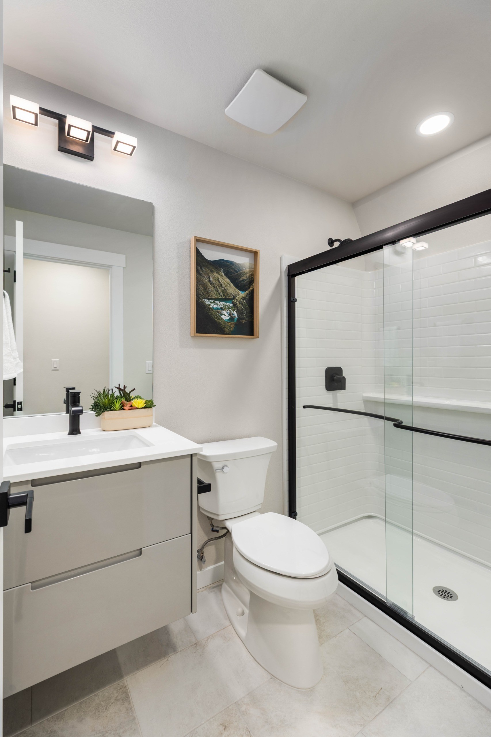 Sleek modern bathroom in a luxury home featuring a floating white vanity, frameless glass walk-in shower, marble-effect tile flooring, and black fixtures