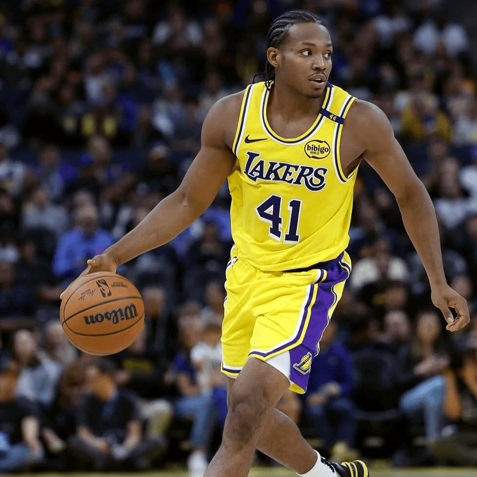 Quincy Olivari in a yellow Los Angeles Lakers uniform, number 41, dribbles a basketball on the court during a game, with spectators visible in the background.