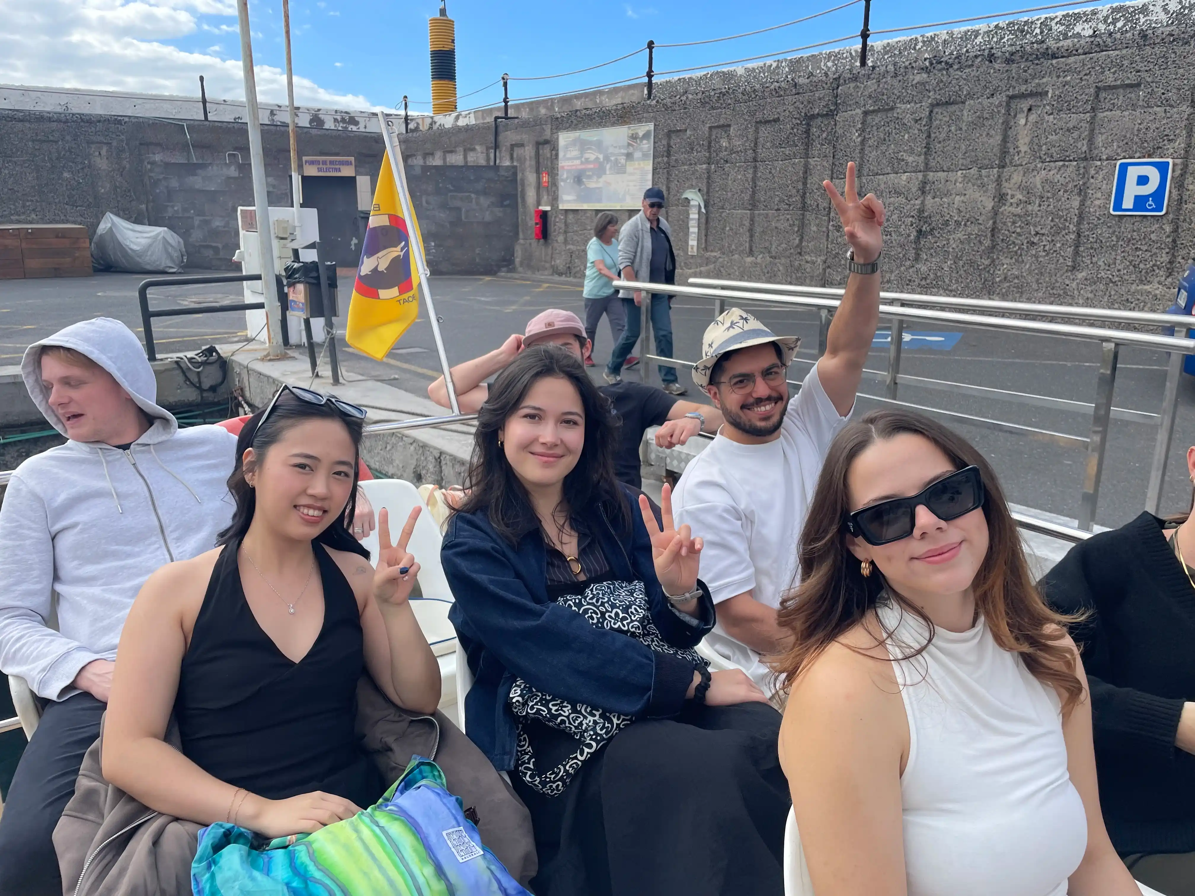 Group of friends making peace signs while sitting on a boat at a dock