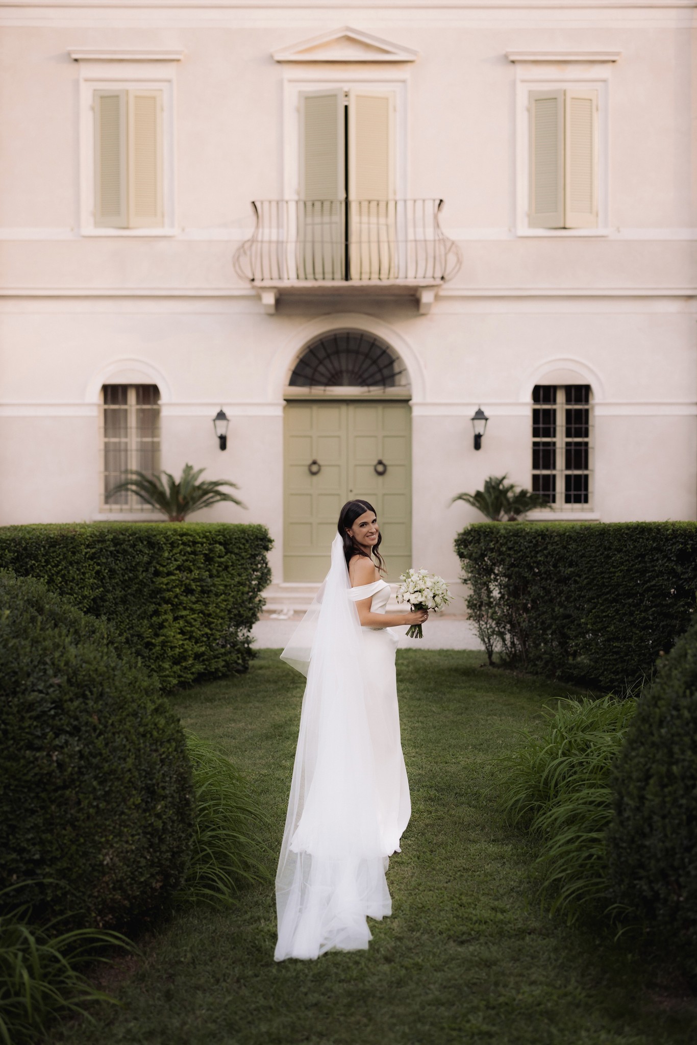 Sposa in abito bianco con velo tra le siepi del giardino di Villa Negri, bouquet in mano, reportage di matrimonio