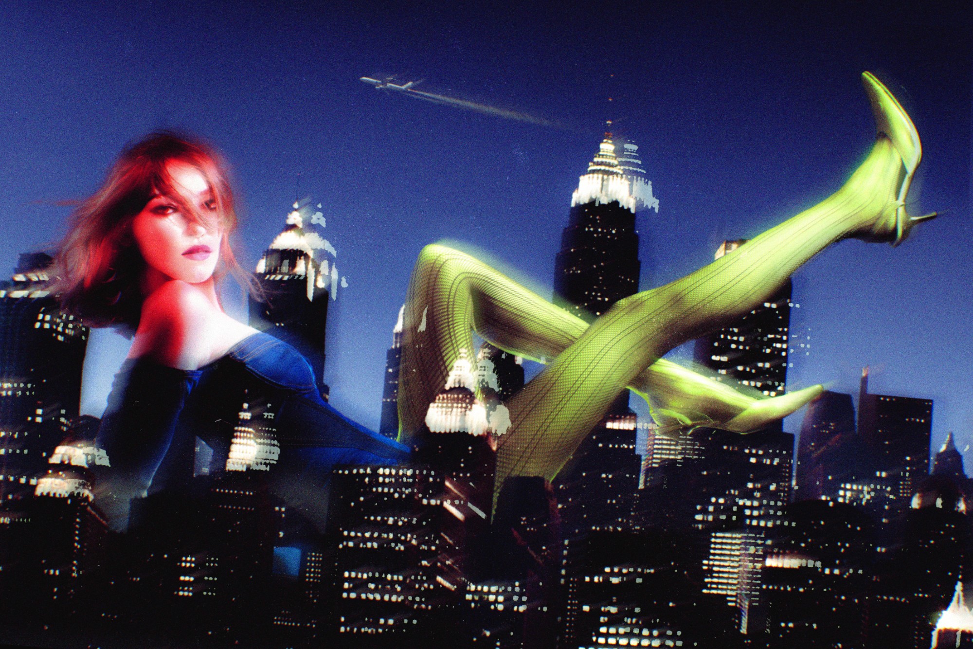 A surreal fine-art photograph by DramatK (Lélio Bazin) featuring a giant woman in a blue corset and neon green tights reclining over a night-time New York City skyline, blending fashion photography with dreamlike architectural elements.