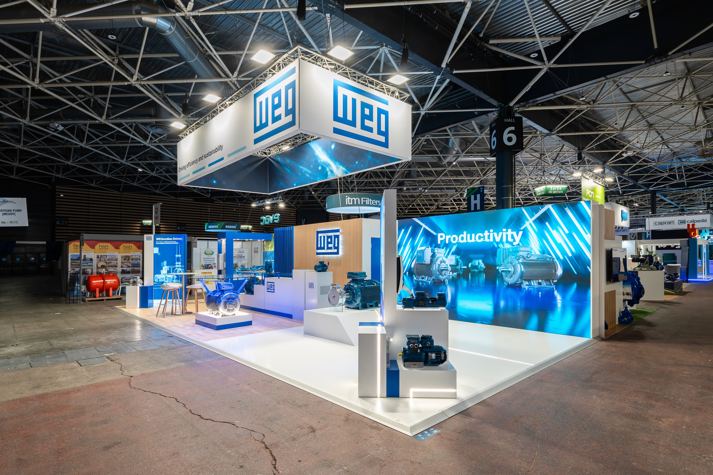 Stand WEG Pollutec 2025 réalisé par Expace – vue frontale du stand avec bandeau lumineux Driving efficiency and sustainability, moteur industriel sur podium vitré rétroéclairé, grands écrans LED et espace lounge bois