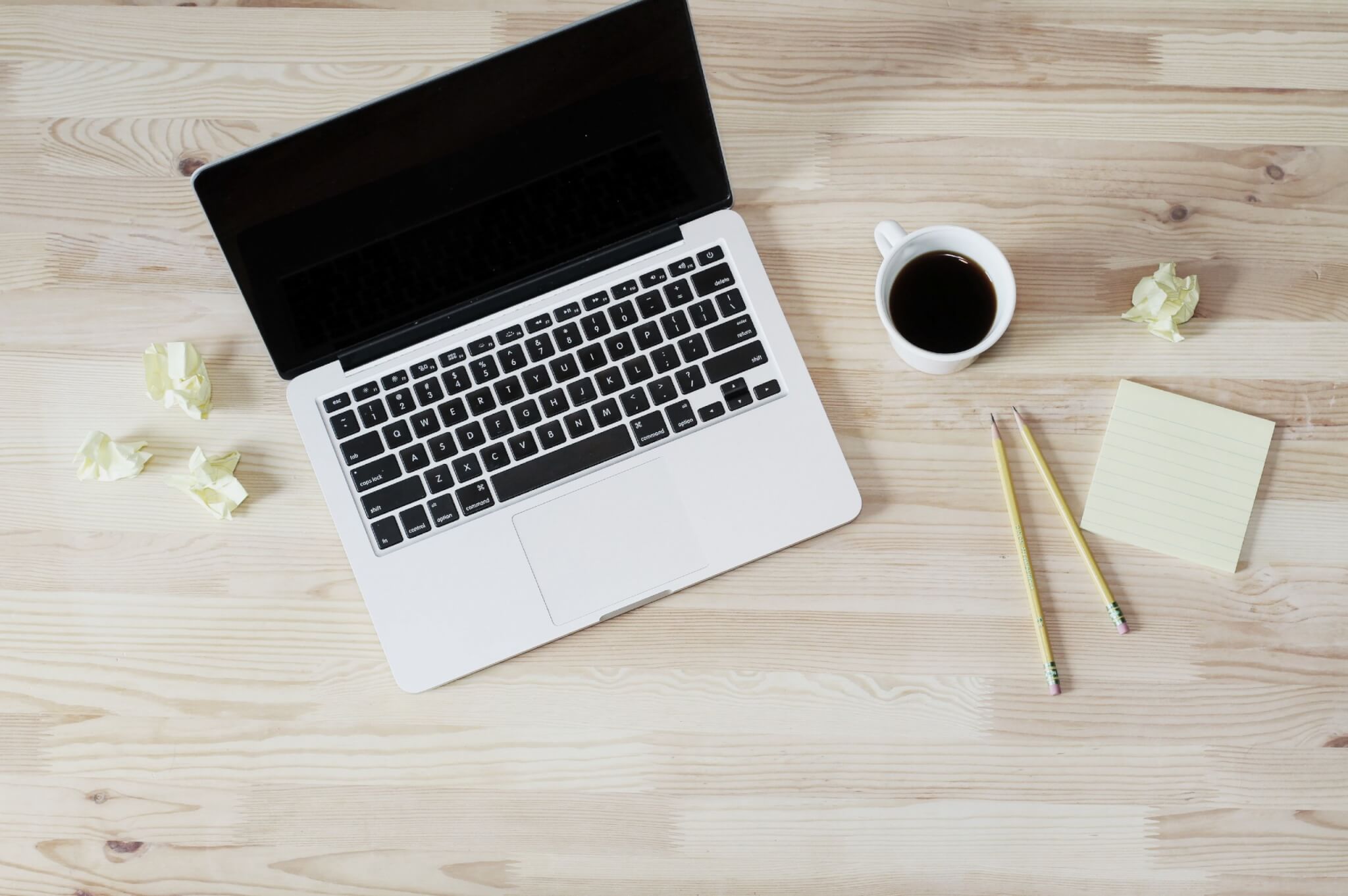 Top-down view of a laptop, coffee cup, sticky notes, and pencils on a minimal home office desk