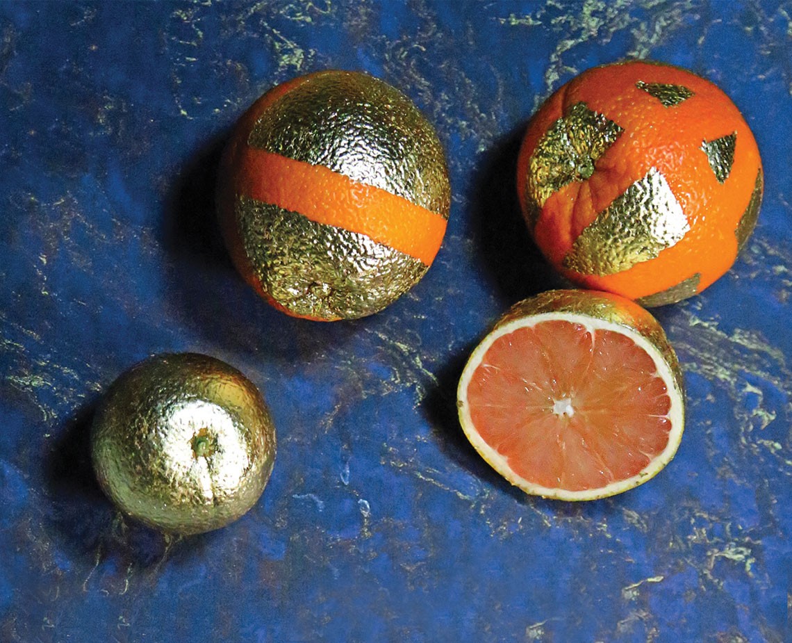 Three spherical objects are arranged on a blue marbled surface. Two are whole: one with an orange band and the other with a textured, metallic appearance. A third is cut in half, revealing its pinkish-red flesh. The objects are positioned in a loose triangular formation.