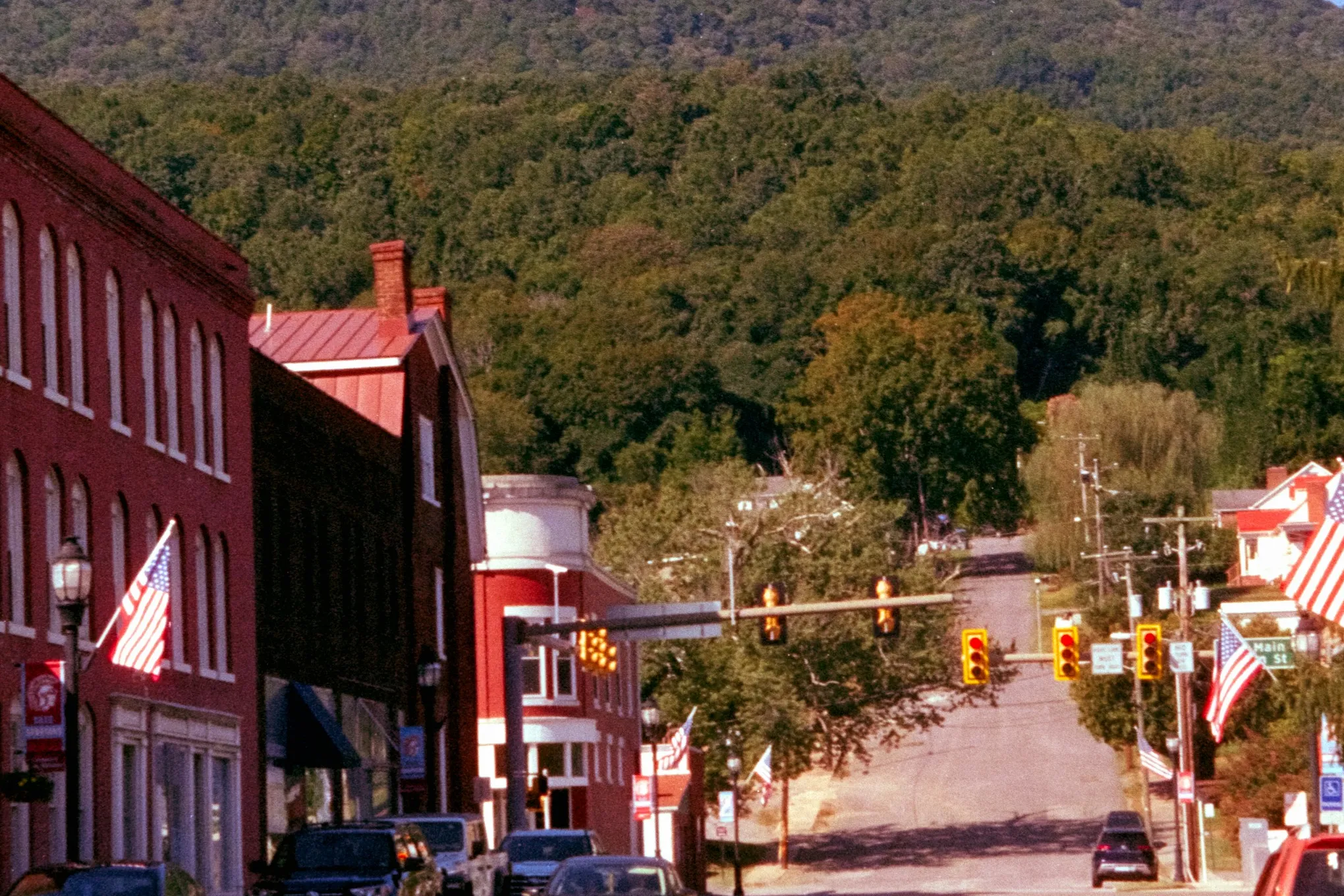 A small-town main street of red brick buildings with a wooded mountain behind