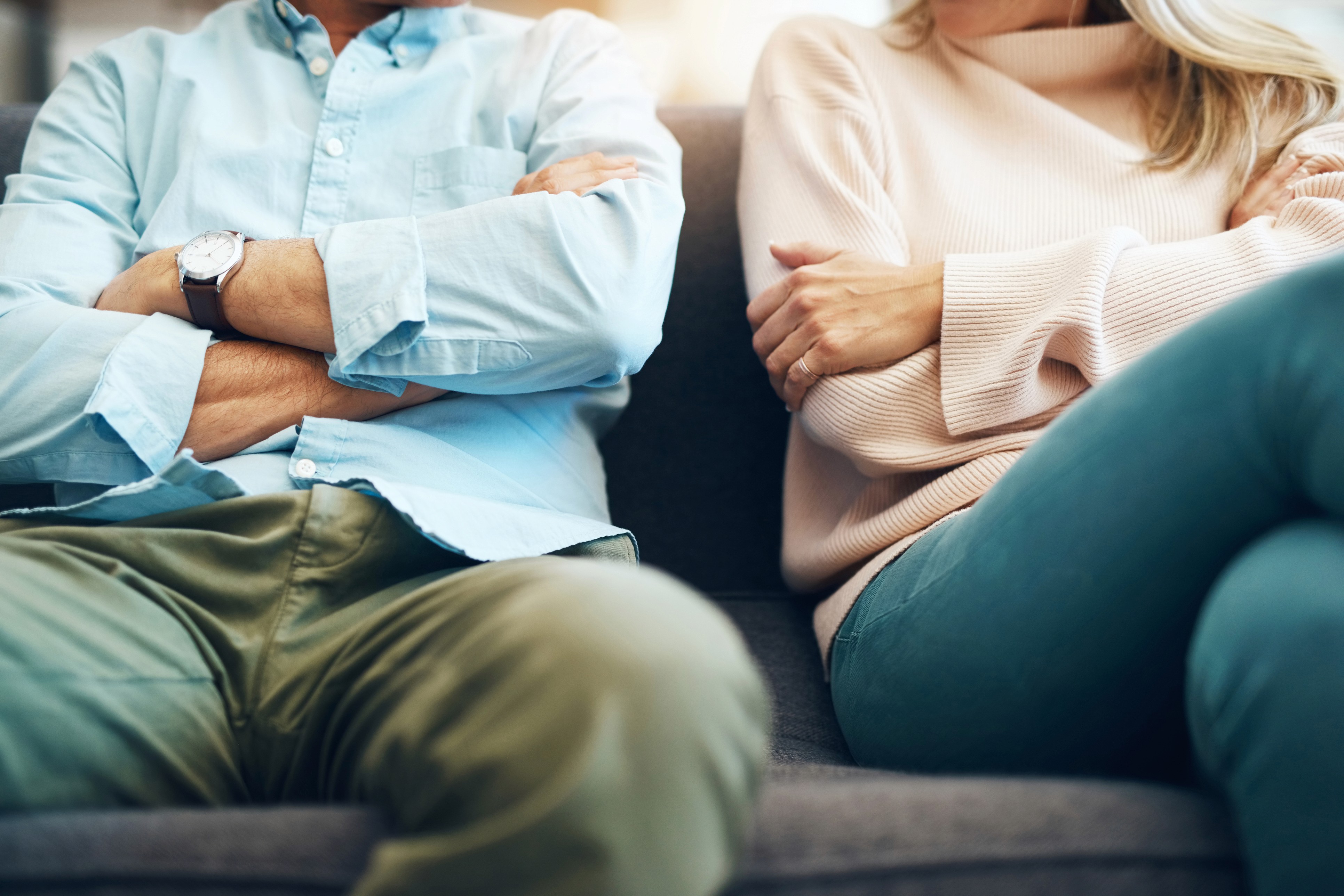 A man and a woman sitting on a couch with their arms crossed
