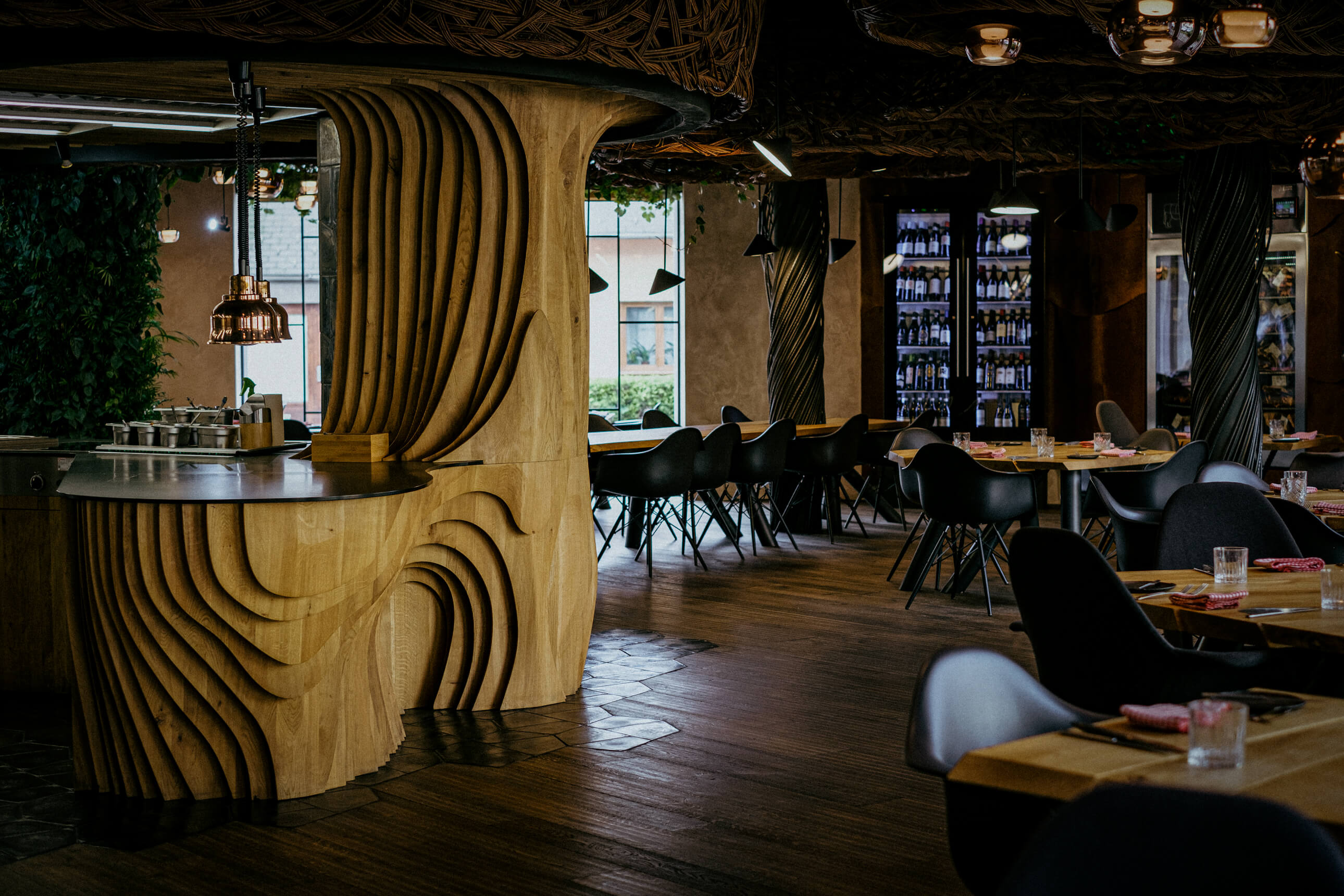 Moderní designový interiér Steak Restaurant Olomouc s organickými dřevěnými prvky, tlumeným osvětlením a vinnou vitrínou v pozadí