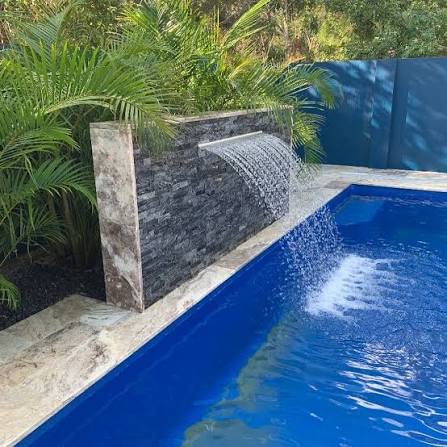 Installation of a stacked-stone water feature for a residential pool, creating a tropical spa atmosphere with lush greenery and a luxury finish.