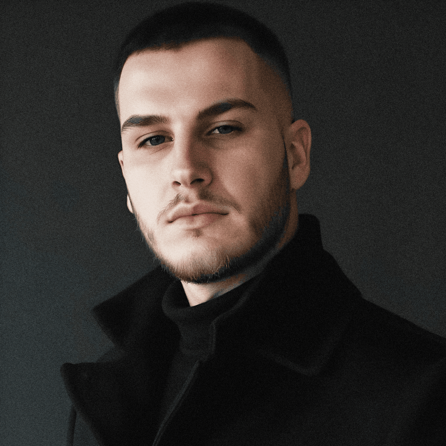 Person wearing a blue puffer jacket and red backpack standing in front of a light blue building on a city street.