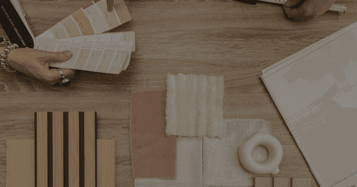 Top view of fabric samples, millwork samples and textural items as designer hands hold measuring tapes and paint chip fans trying to determine what works best.