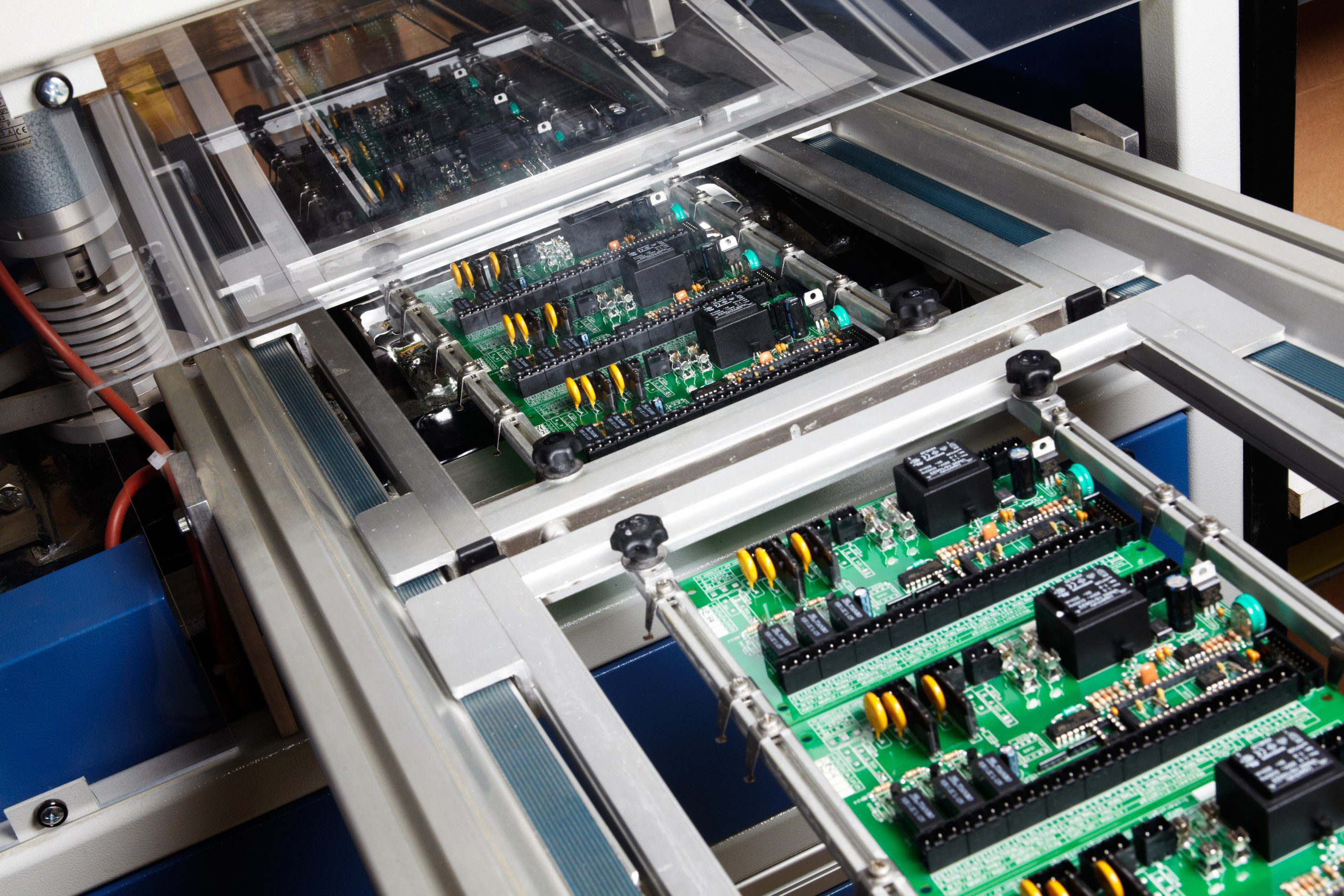 Green printed circuit boards on an automated assembly conveyor in an electronics factory.