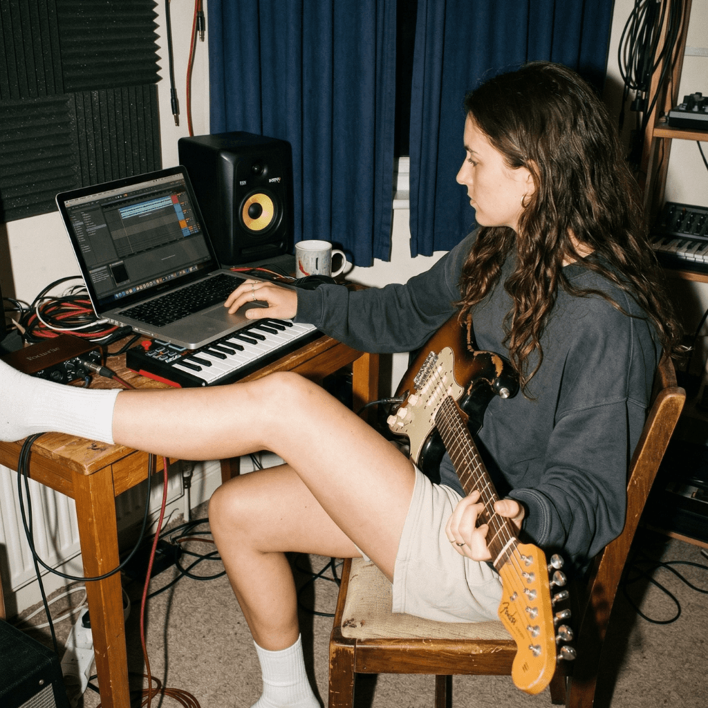Persona tocando guitarra en estudio casero con equipo de grabación
