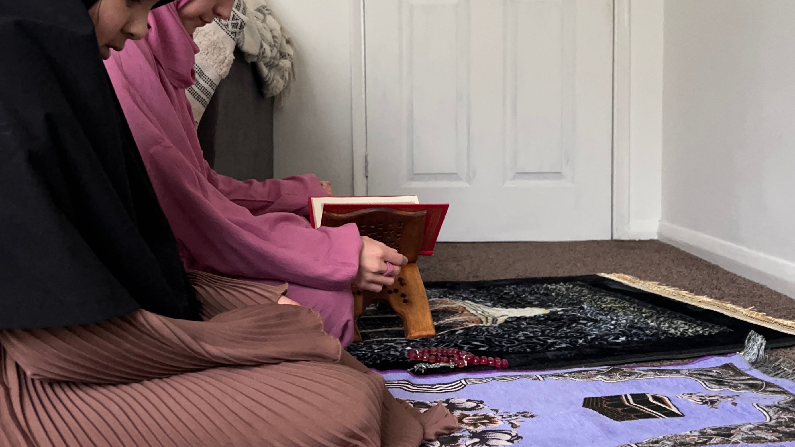An image showing 2 women praying on a namaz mat and reading quran