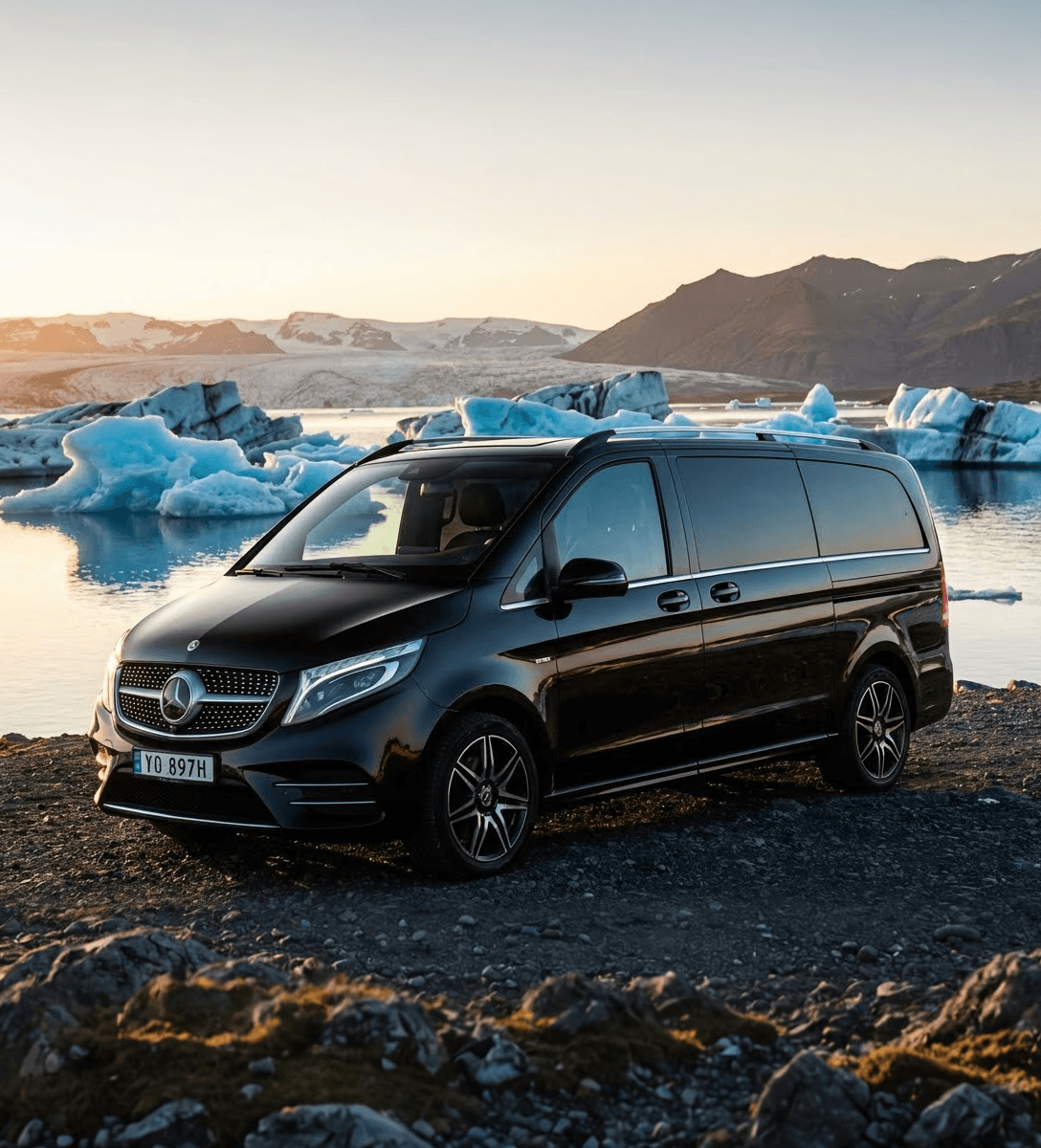 Black Mercedes van parked by the water against a glacier and mountains.